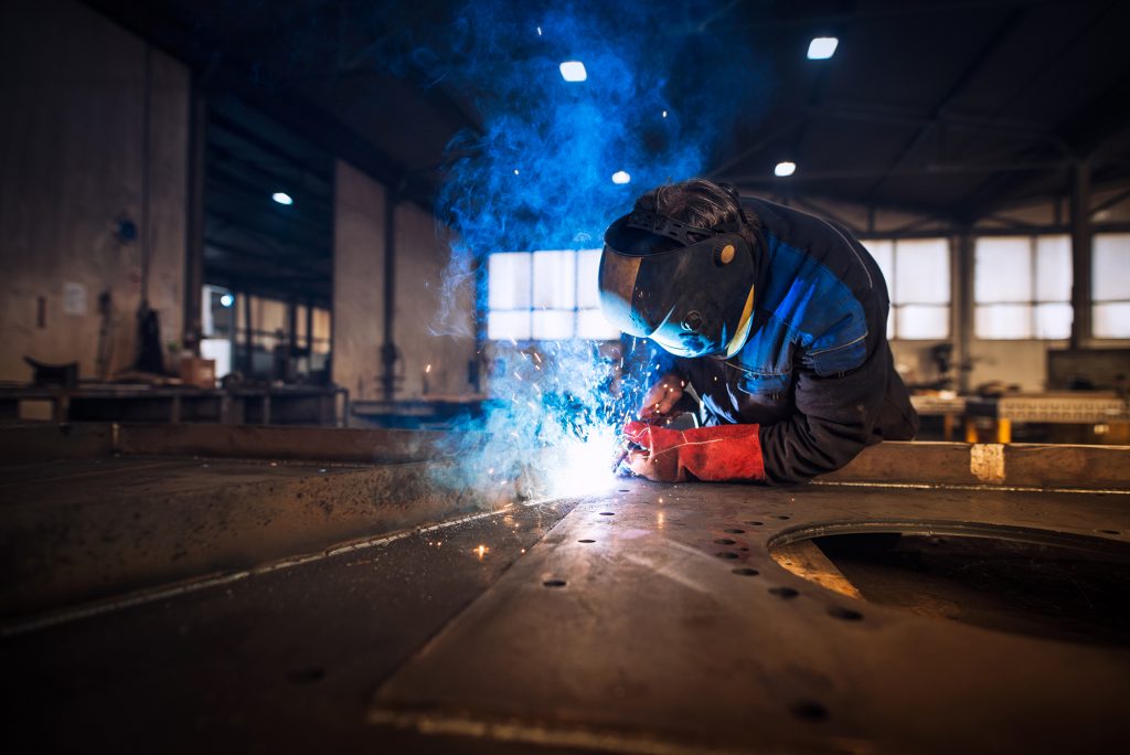 Close up view of worker welding metal construction in industrial workshop.
